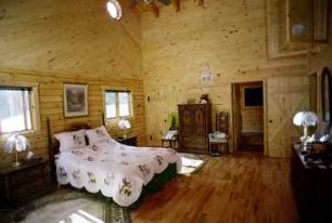 Log home bedroom with pine walls, a hardwood floor, and a quilted bed
