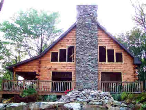 Custom log home with a tall stone chimney and covered deck